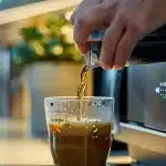 a person pouring a cup of coffee from a coffee machine in an office break room, provided by mucn vending coffee service